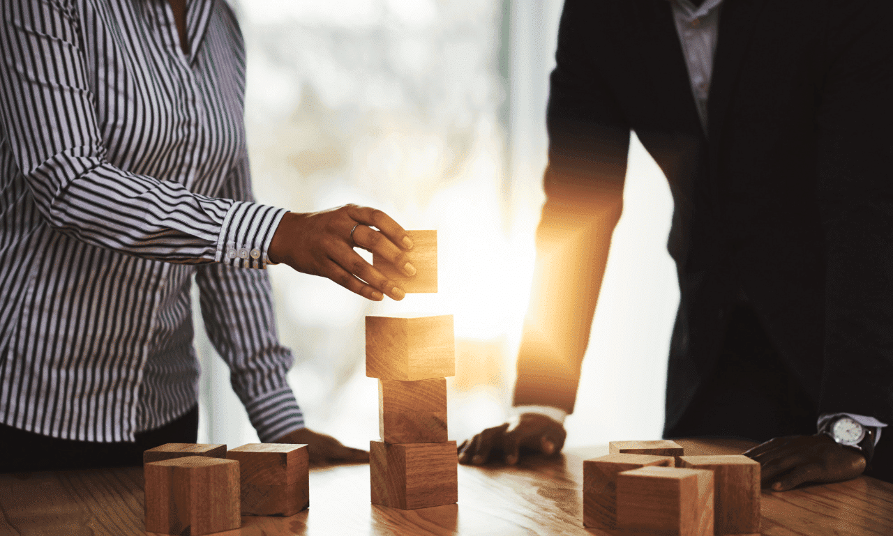Two professionals stacking wooden blocks, symbolizing teamwork and building a strong financial foundation.