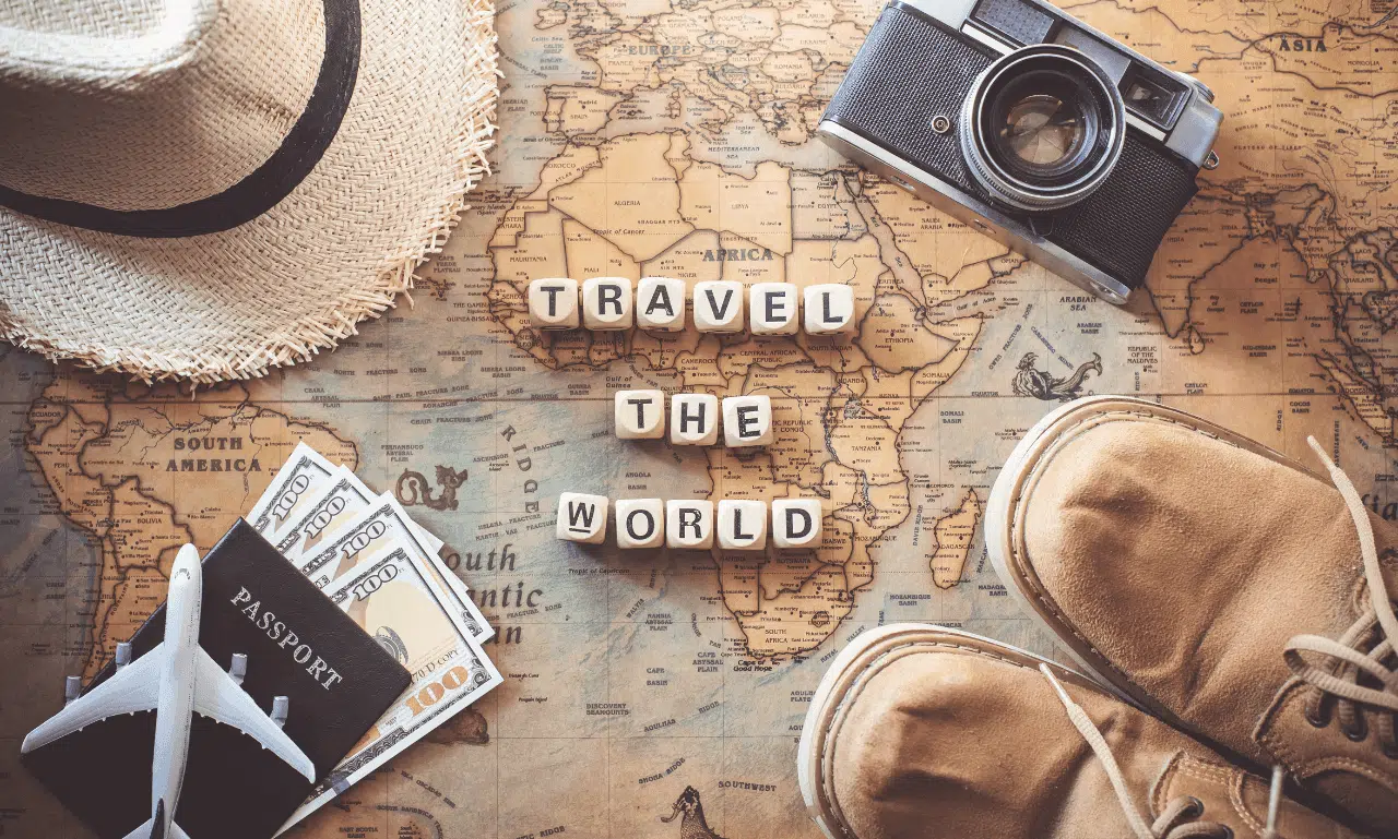 Flat lay of travel essentials including a world map, passport, camera, and accessories, symbolizing global travel and adventure.